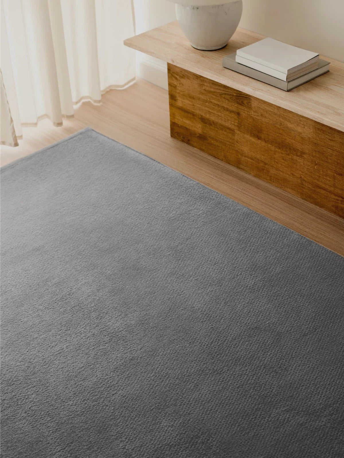 Minimalist interior featuring a soft gray plain rug, a natural wood bench, and a neutral-toned decor for a sleek and modern aesthetic.