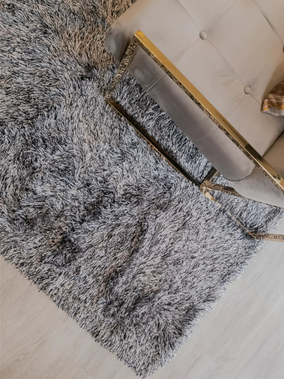 Plush gray 4x6 area rug with a shaggy texture placed under a modern tufted sofa and a gold-accented glass coffee table on a light wood floor.