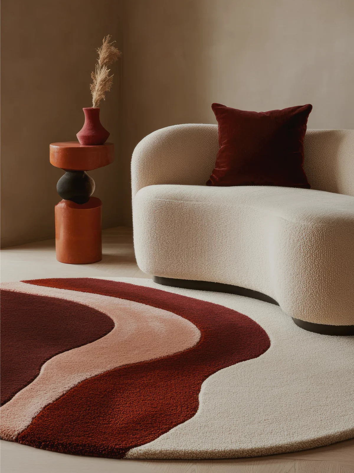 Modern living space featuring an abstract rug with wavy burgundy, blush, and cream tones, paired with a curved boucle sofa and sculptural accent table.